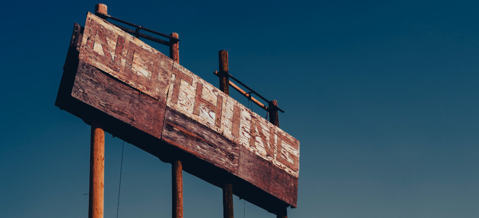 An faded wooden sign that says the word 'Nothing' in large blocky letters, set against a clear blue sky. Photo by Evan Buchholz on Unsplash.com